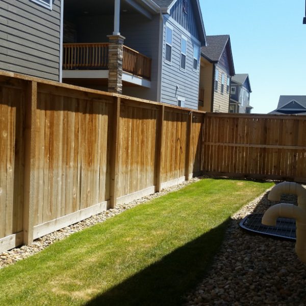 A narrow back yard with fence and grass and rock