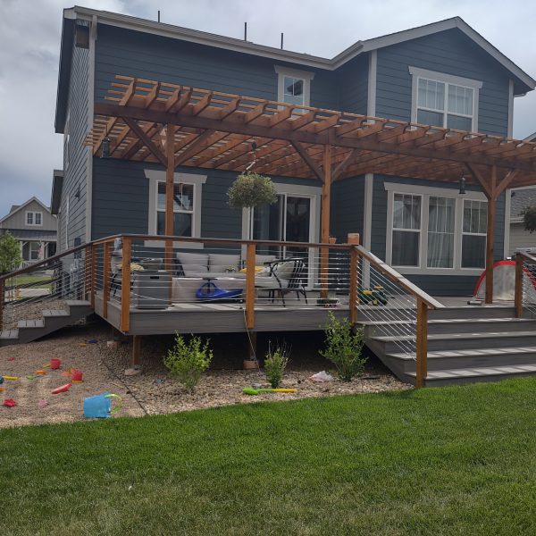 blue house with big deck, pergola and steps to lawn.